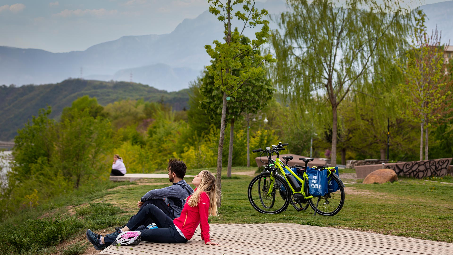 A couple is sitting resting along the Eisack river on the Bolzano Promenades after a bike ride. 
