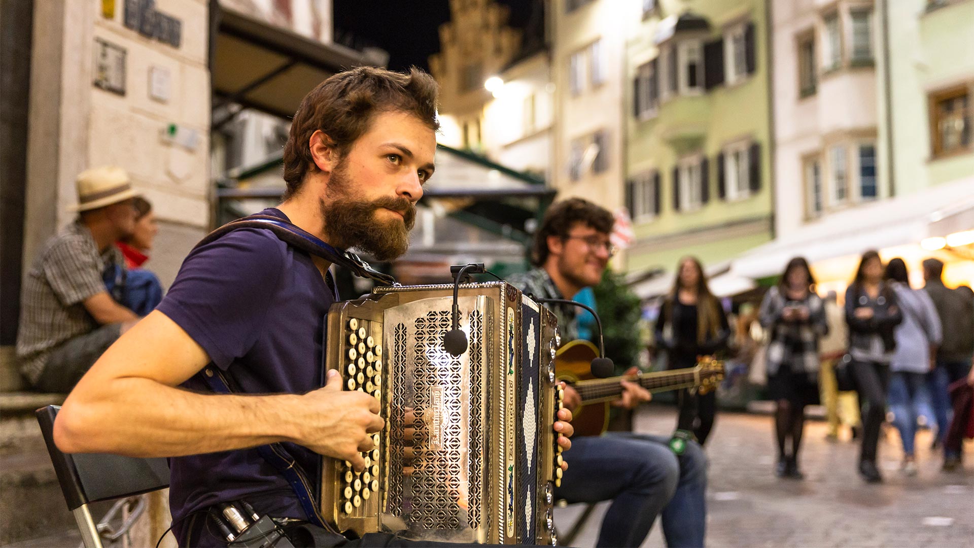 A young boy, a member of a music group, is playing his accordion in the historic centre of Bolzano. 