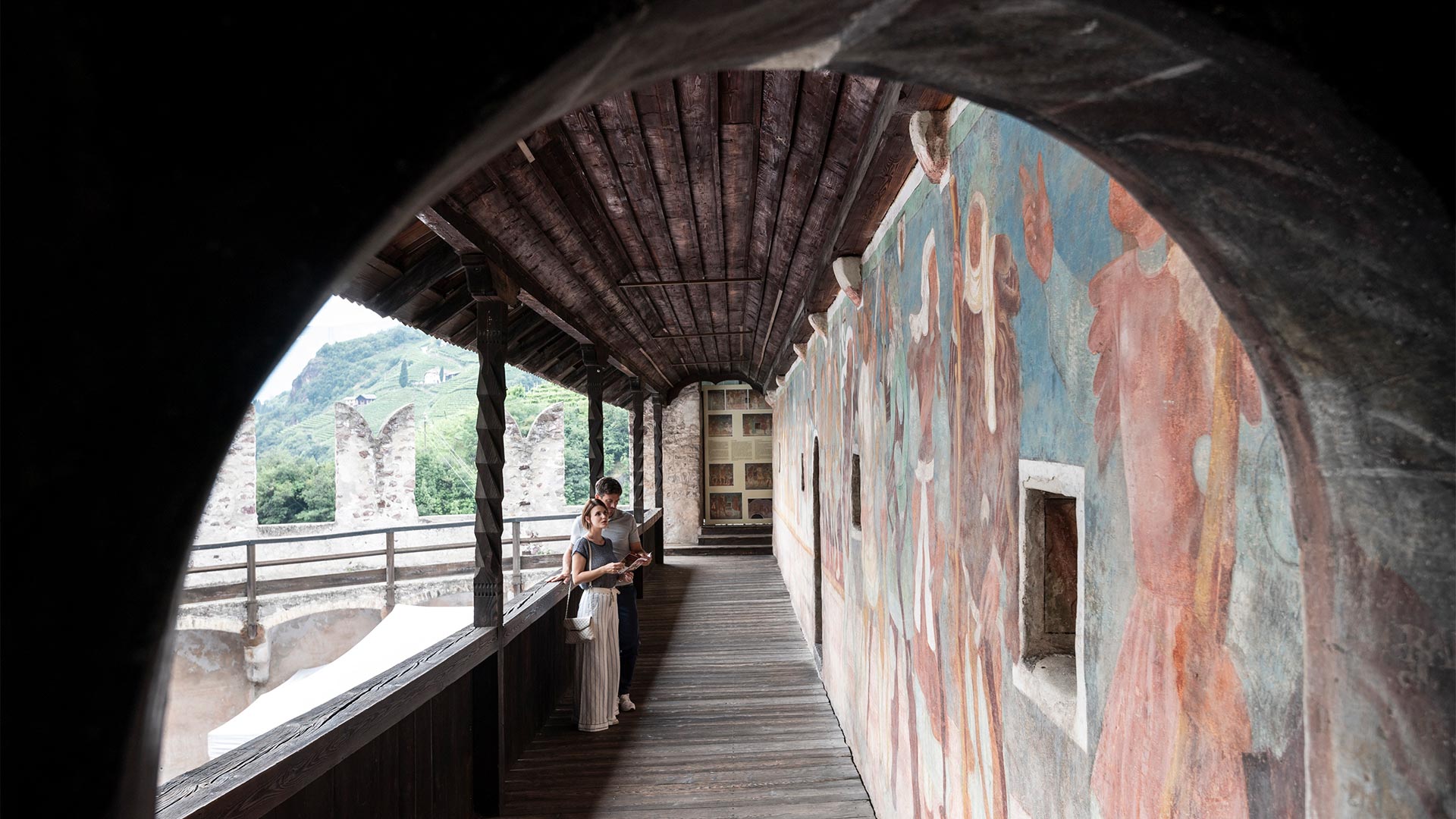 Una coppia sotto un antico porticato di Bolzano osserva gli affreschi con in mano dei depliant.