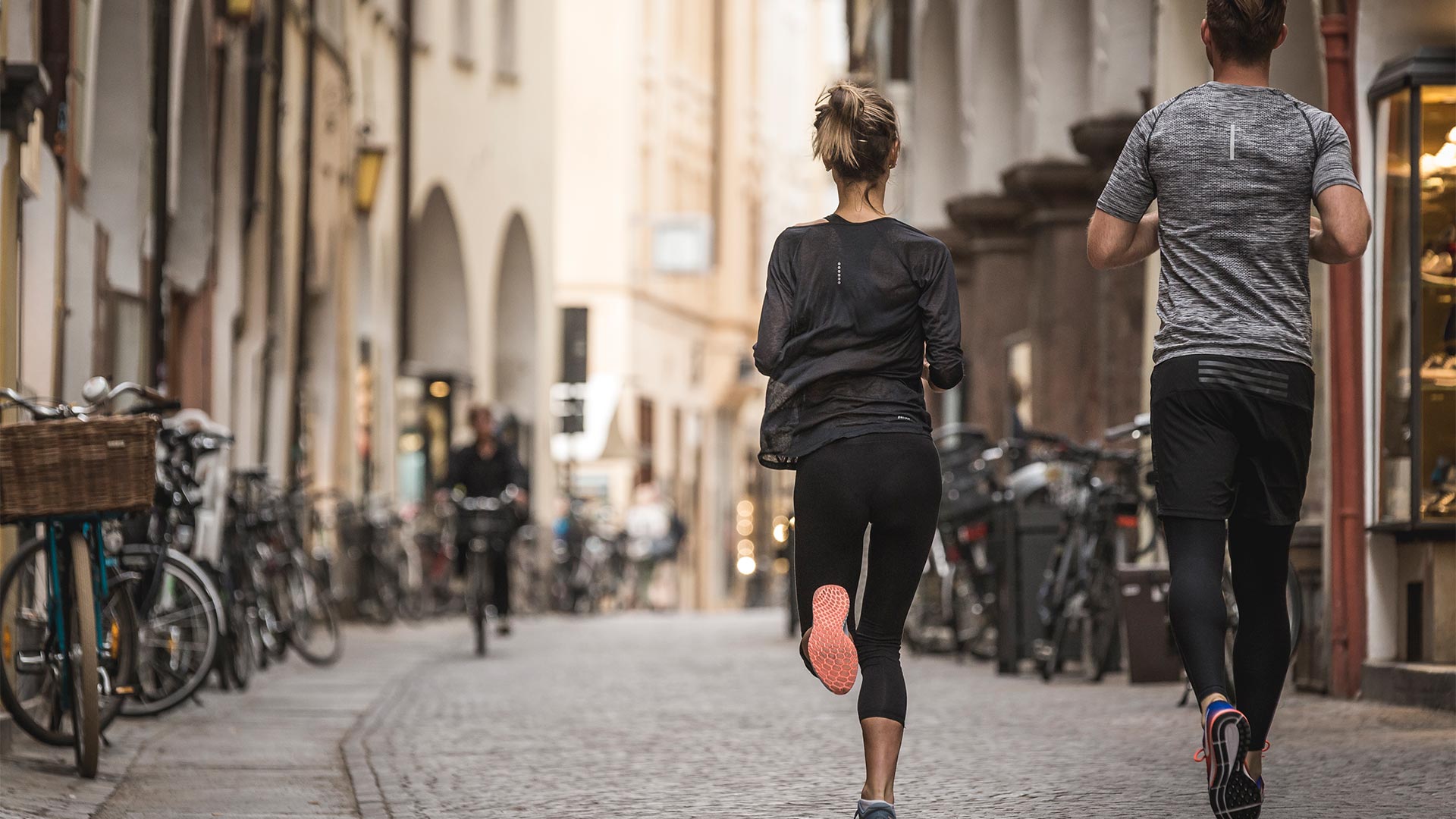 A couple in love are exercising in the streets of Bolzano's old town. In front of them a cyclist is cycling in the opposite direction.