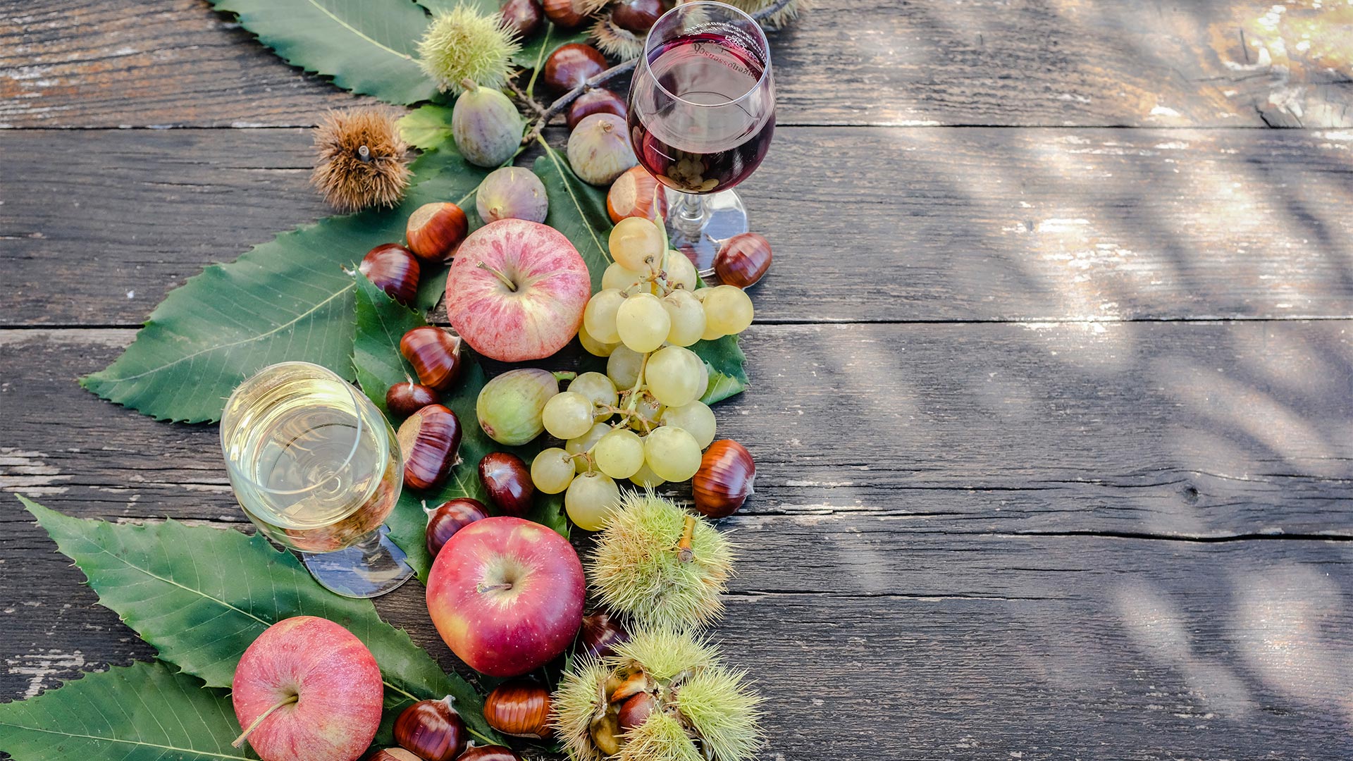 A seasonal dish of red apples, grapes and chestnuts accompanied by a glass of white wine.