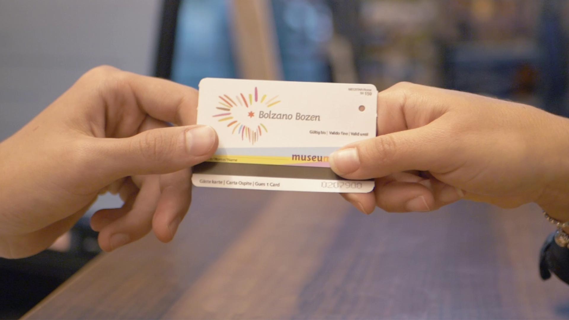 Im Vordergrund die Vorderseite der Guestcard für die Aktivitäten im Museum mit dem Schriftzug "Bolzano Bozen" in der Mitte und dem zu scannenden Balken darunter.
