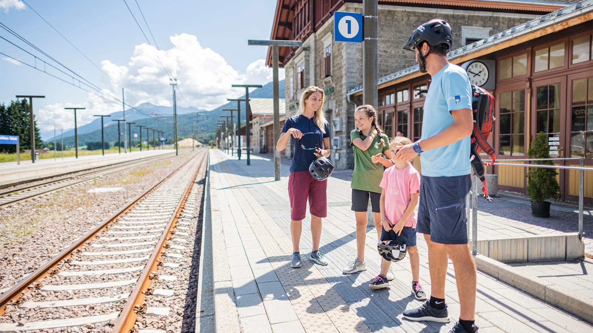 A family, who have finished their activities on their bicycles, is standing at the railway station waiting for the train to arrive.