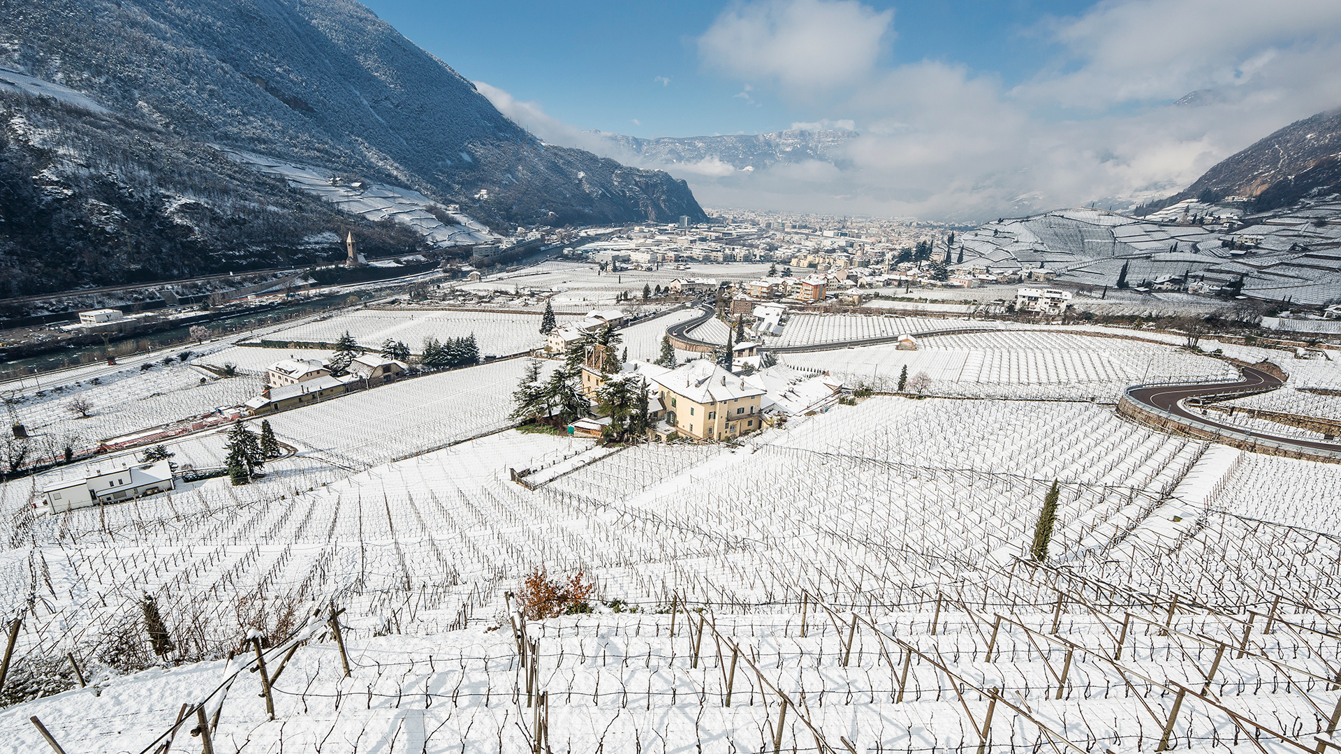 Winterlandschaft an einem sonnigen Nachmittag in Bozen, wo die Weinberge und Dörfer mit Schnee bedeckt sind.