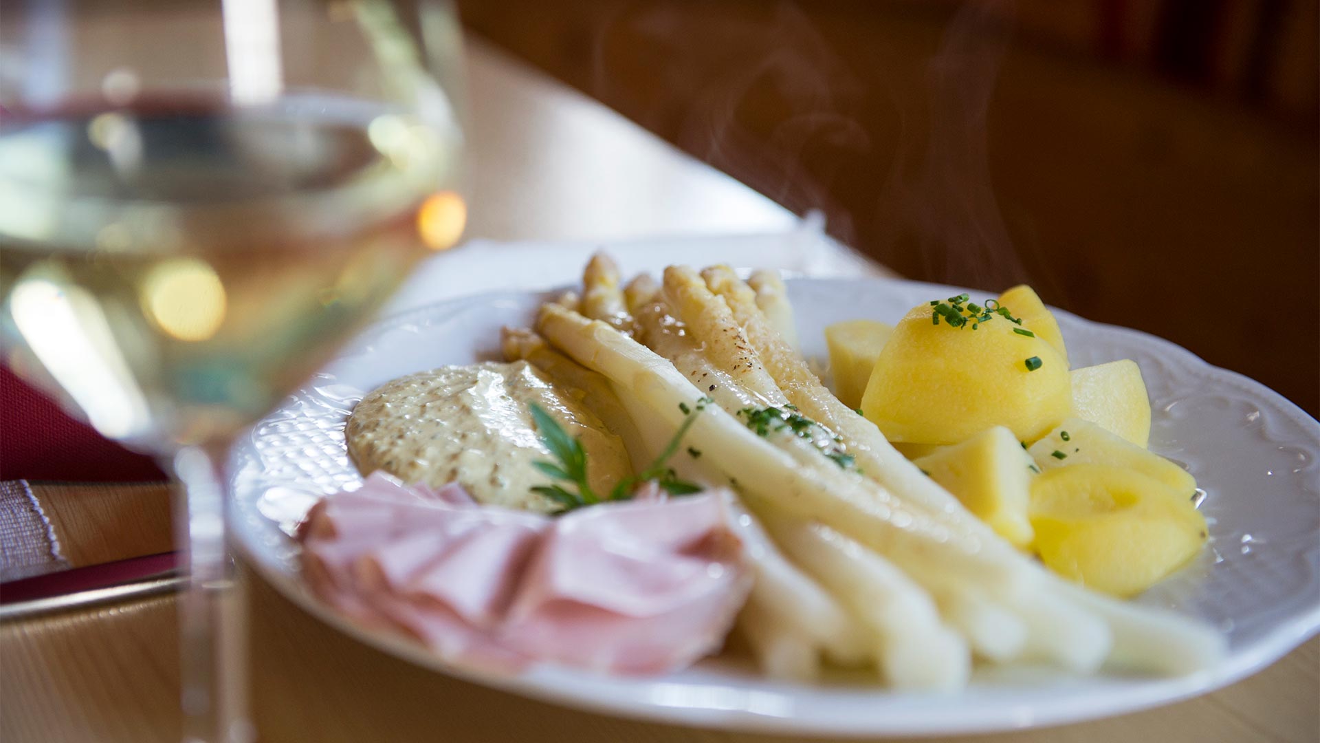 Ein typisches Südtiroler Gericht aus gekochtem Spargel, Salzkartoffeln und Schinken, serviert mit einem Glas Weißwein.