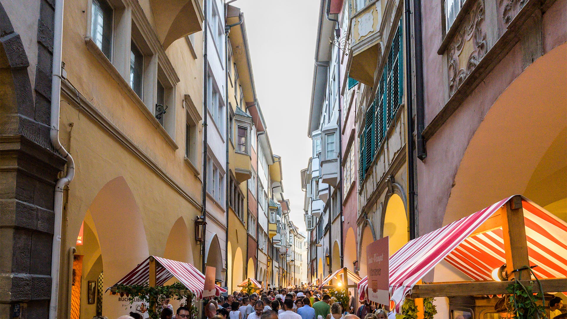 Enge Gasse zwischen den Arkaden im historischen Zentrum von Bozen, die mitten in einer Veranstaltung von Touristen und Bürgern bevölkert wird.