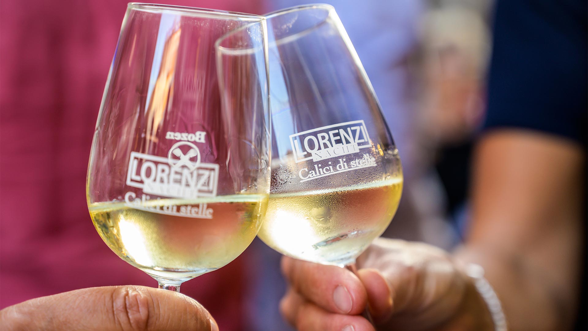 In the foreground a toast between two participants of a traditional event with glasses of white wine.