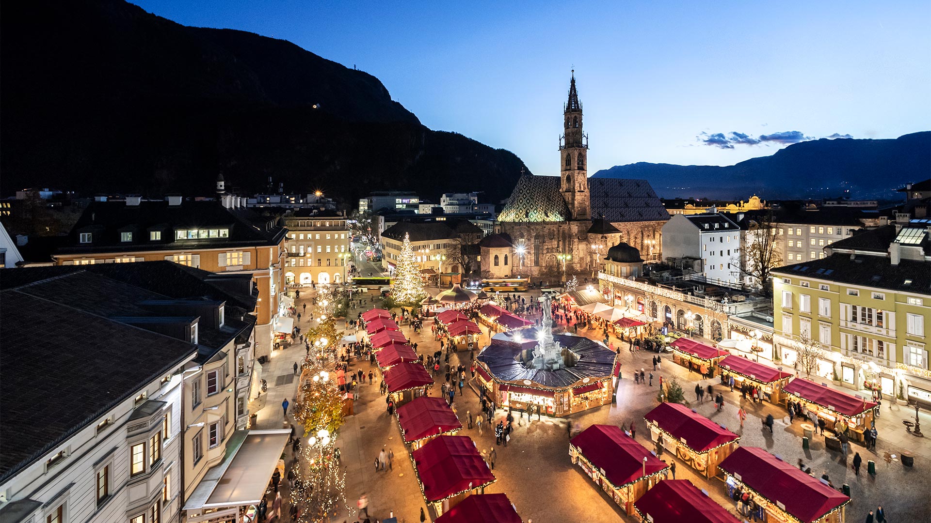 A view of Piazza Walther from above on a winter's evening, where the Christmas markets occupy the square and crowds of shoppers are intent on shopping. 