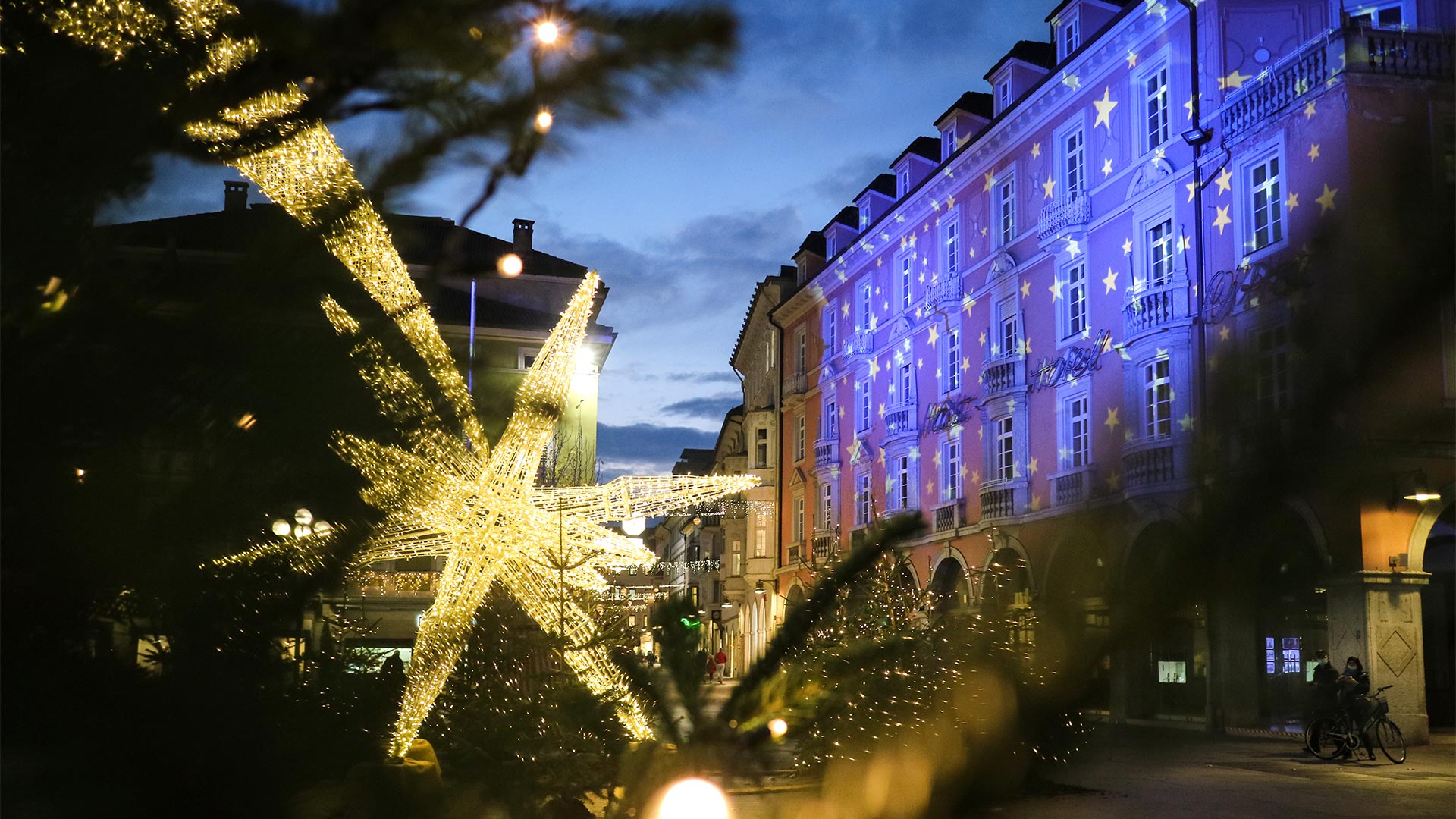 Bozen an einem Weihnachtsabend mit einer sternförmigen Leuchte auf dem Waltherplatz und festlich beleuchteten Gebäuden.