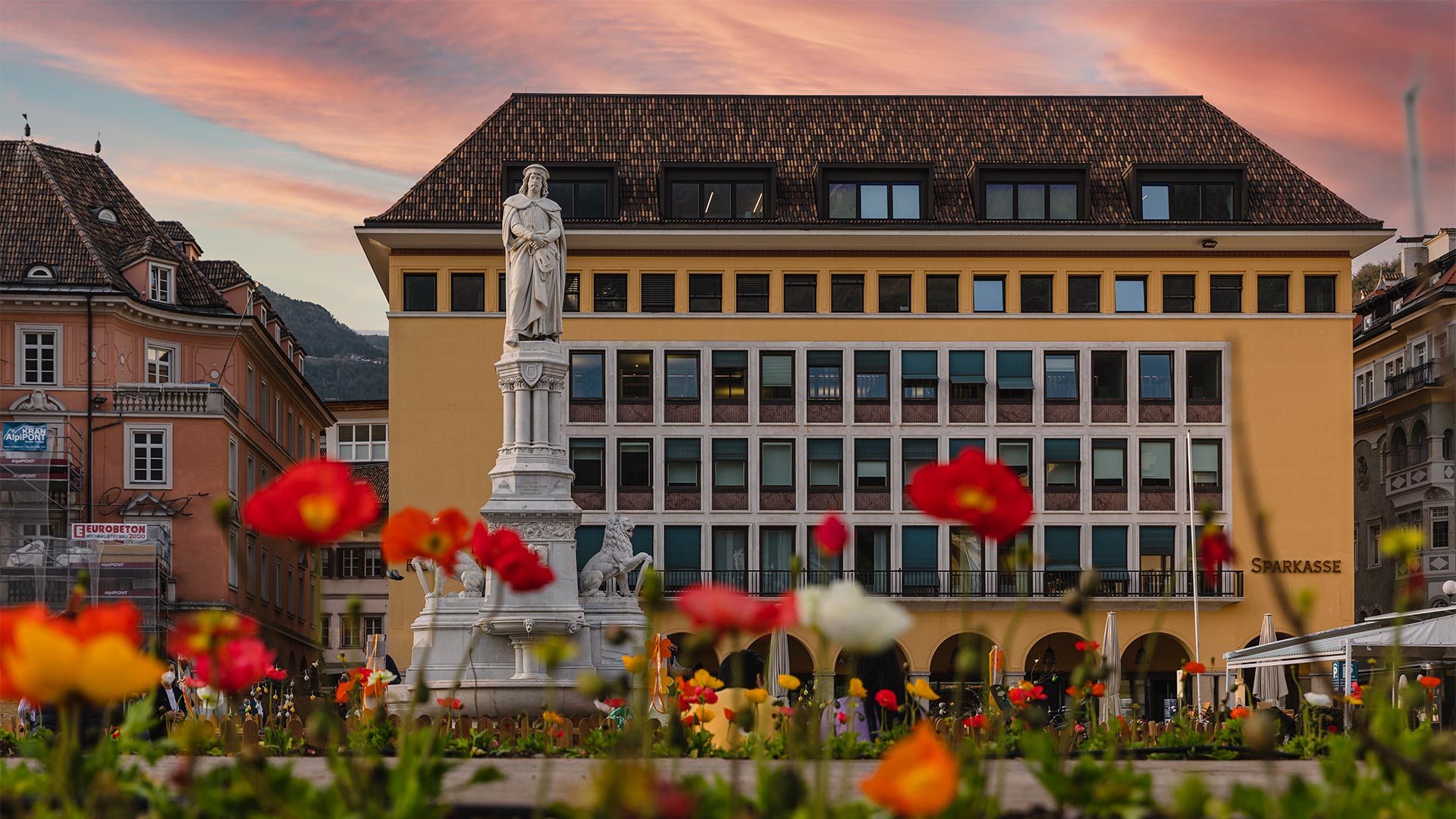 Vista frontale di Piazza Walther con la statua in primo piano davanti agli edifici storici in un tramonto di primavera.