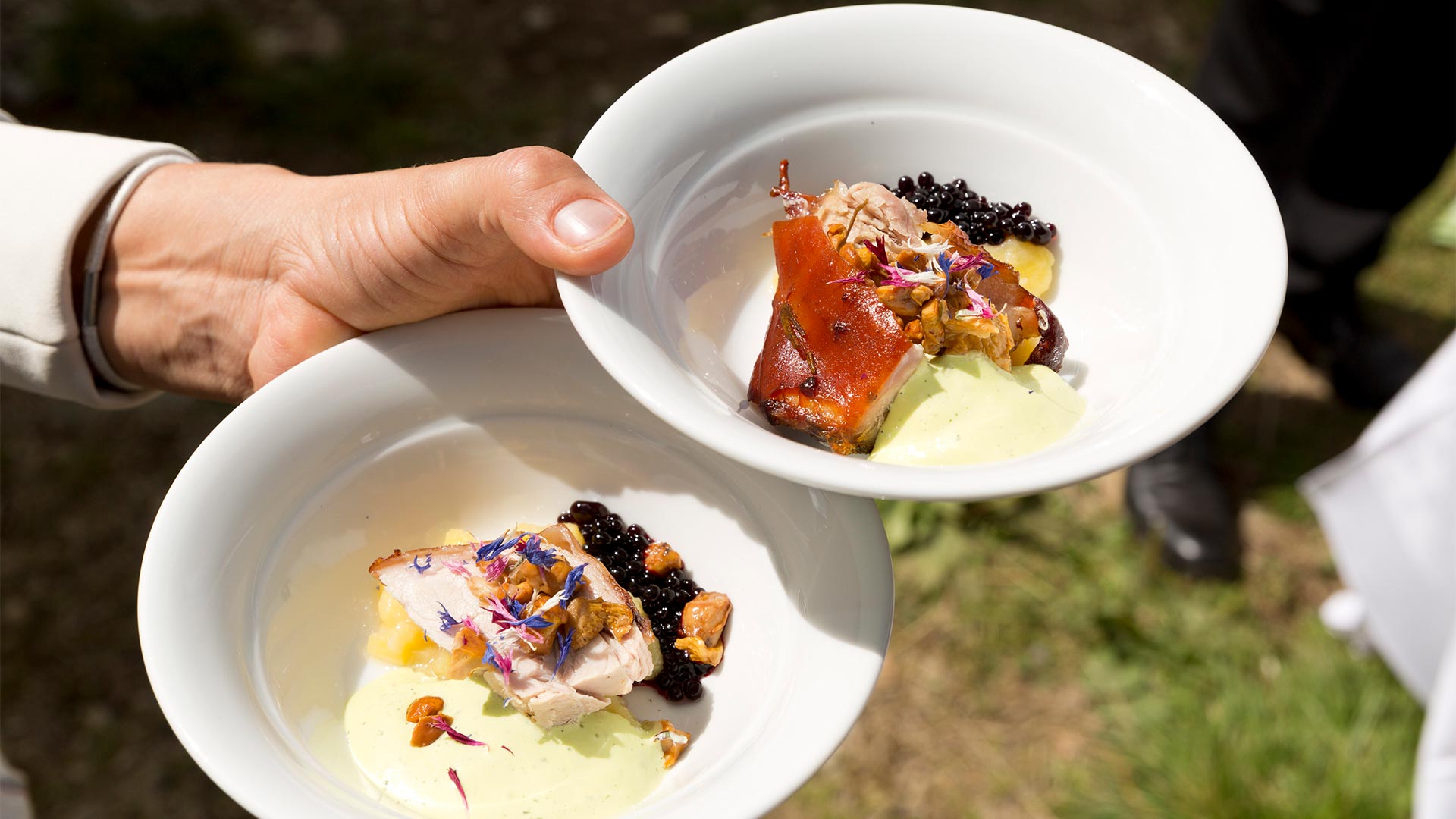 The hand of a waiter holding two typical Bolzano dishes of meat and vegetables.