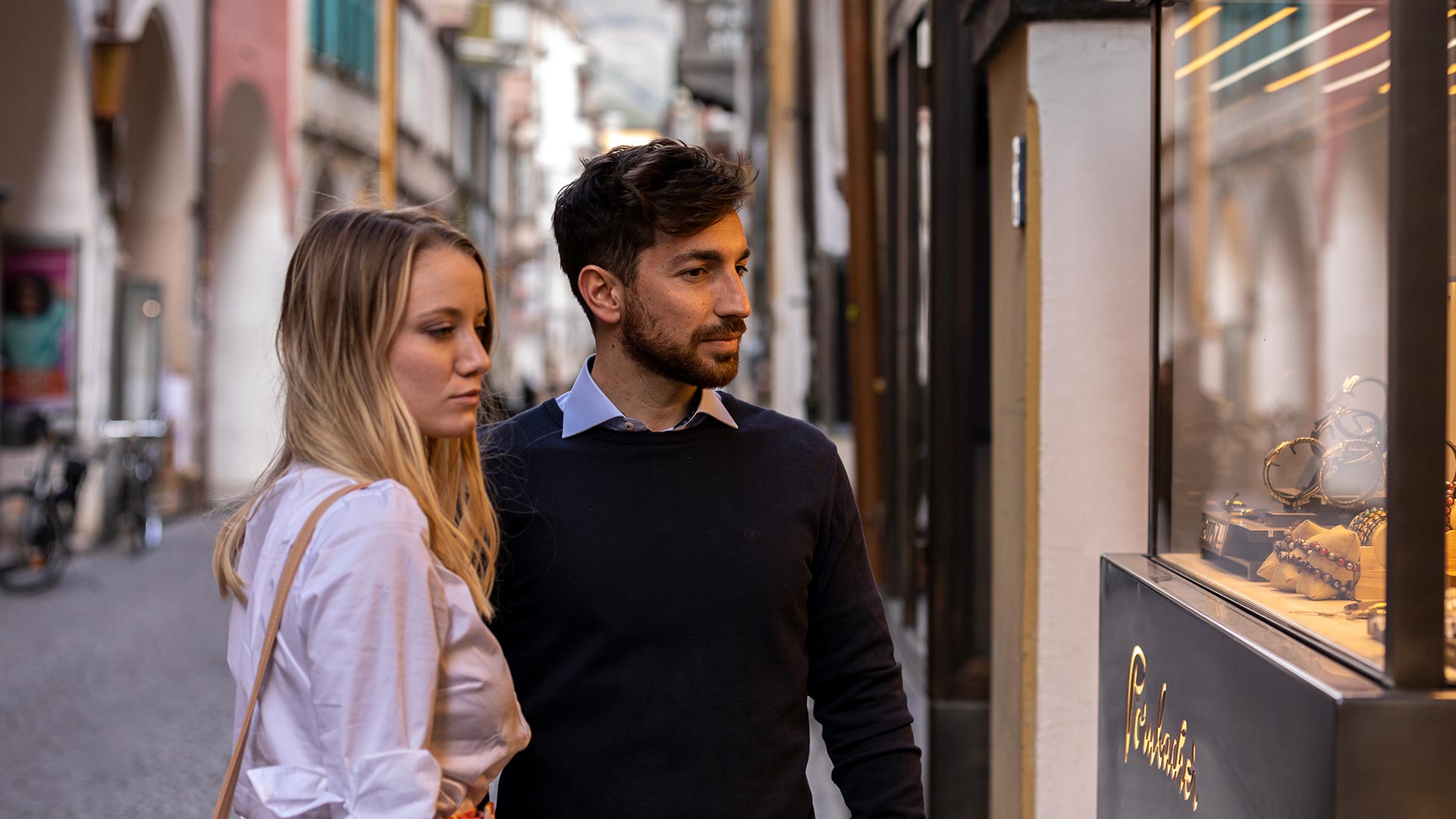 An engaged couple goes shopping and stops to look at the window of a jewellery shop in the centre of Bolzano.