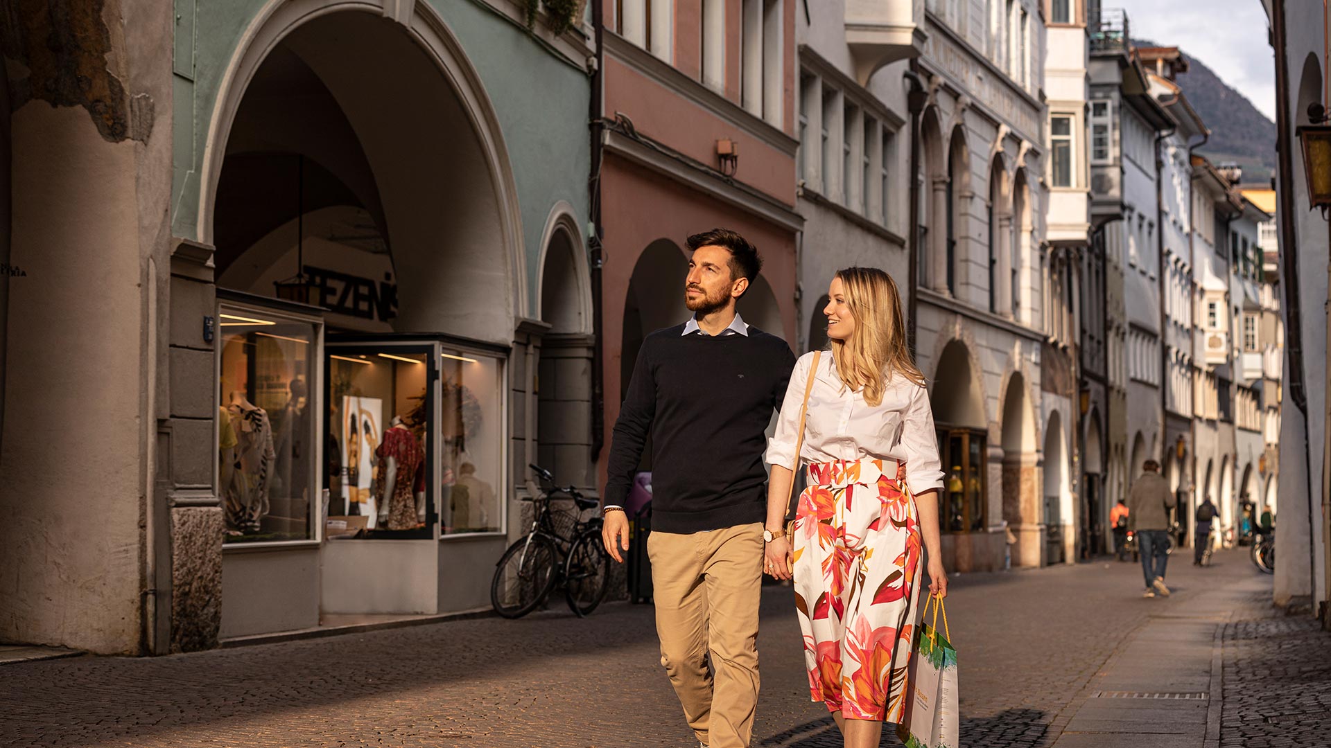 Ein Einkaufspaar schlendert durch die Lauben im Zentrum von Bozen und bewundert die Schaufenster.