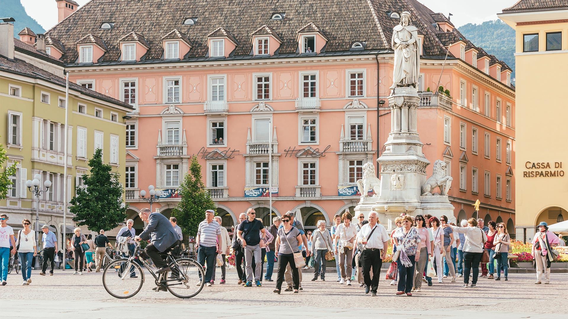 Photograph of the crowds of citizens moving, both on foot and by bike, around Piazza Walther on a sunny day.