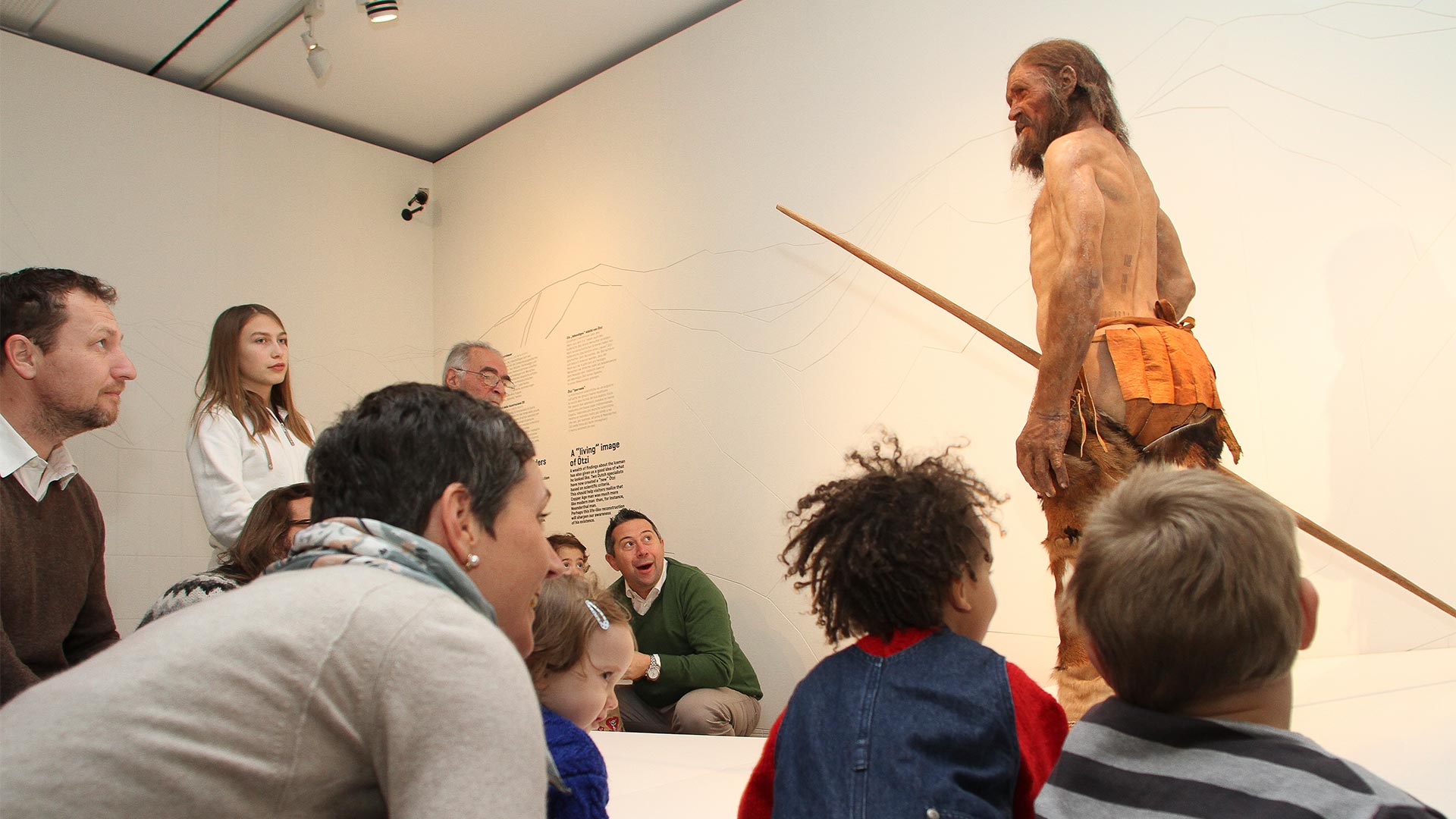Nel museo di Ötzi delle famiglie di giovani e adulti sono sedute in cerchio e ammirano la riproduzione su scala naturale dell'uomo delle nevi.